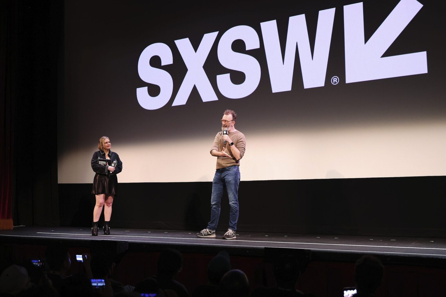 AUSTIN, TEXAS - MARCH 14: (L-R) Claudette Godfrey and John Carney speak onstage during the premiere of "Power Ballad" during SXSW at The Paramount Theatre on March 14, 2026 in Austin, Texas. (Photo by Robin Marchant/Getty Images for Lionsgate)